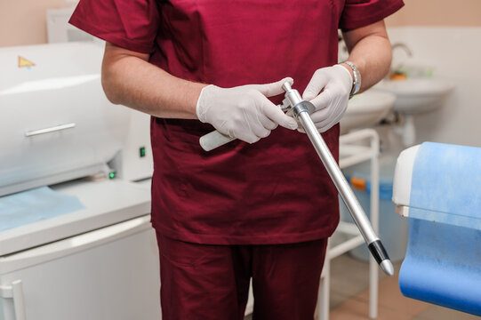 A gloved healthcare professional meticulously holds a silver proctoscope in a clinical setting. Anoscopes with ring lights in the hands of a doctor. Reusable Proctology Instruments