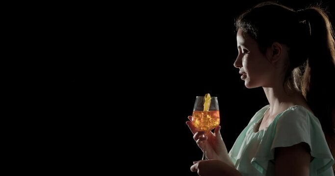 Young woman drinking tasty aperol spritz cocktail on black background