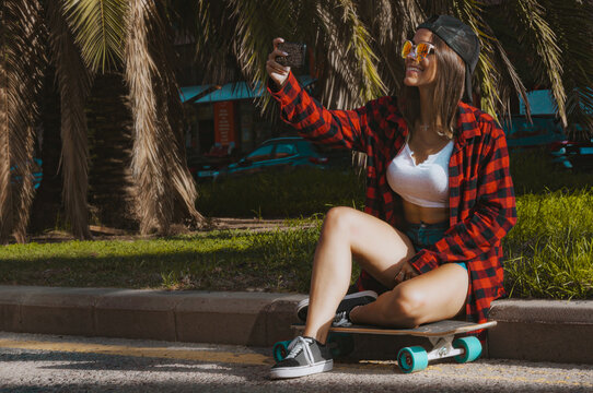 Skateboarder girl takes a selfie sitting on the street. Side image