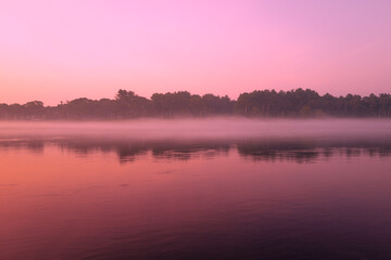 Pink sunrise over the Cape Cod Canal. Symmetrical reflections of the sky and forest over the water surface. 