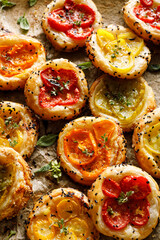 Mini tomato puff pastry tarts with different varieties of tomatoes and herbs, top view. Tasty vegetarian meal.