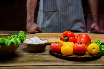 a wooden bowl of flour and vegetables on the kitchen table. man in an apron.