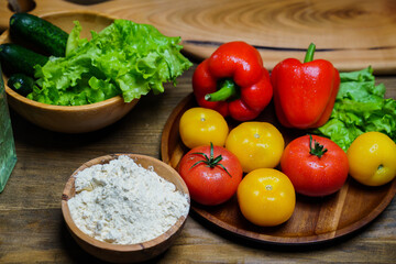 a wooden bowl of flour and vegetables on the kitchen table.