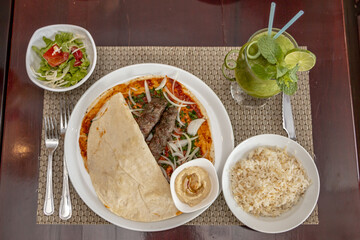 Middle Eastern meal composed of pita, kebab, salad, hummus, rice and a glass of green smoothie