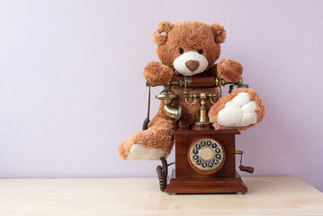 Retro telephone with handset, rotary dial and stuffed toy teddy bear on it