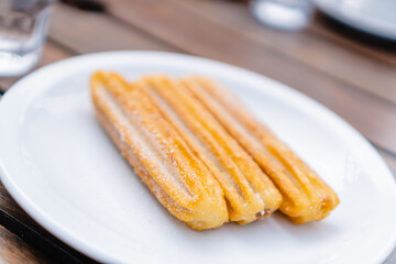 3 Argentinian churros on a plate, in a restaurant outdoors