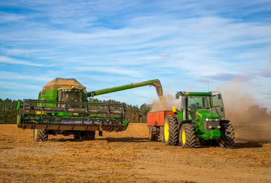 Darfield, Canterbury, New Zealand - January 25 2021: A John Deere 9650 combine harvester unloads barley into the bins behind a tractor in a field in summertime