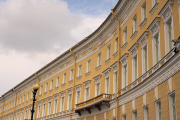 The yellow wall of an old multi-storey building with a cloudy sky in the background.