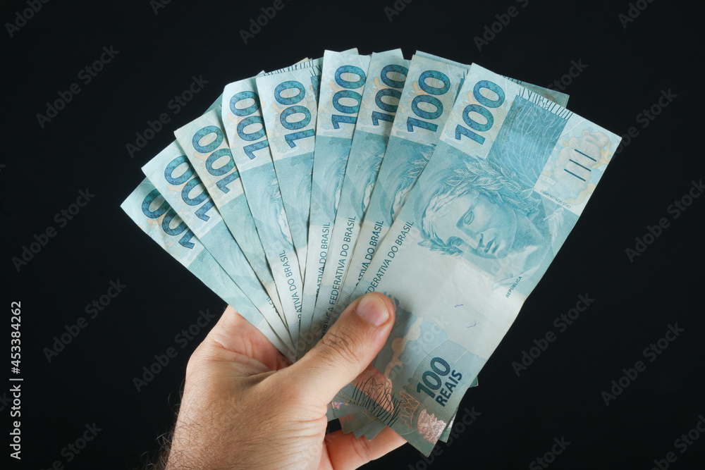 Wall mural hand holding brazilian money. 100 reais banknotes. black background