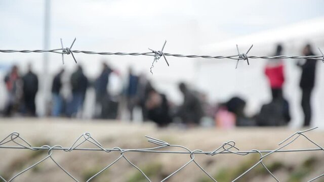 Barbed wire in refugee camp. Migrants behind chain link fence in camp. Group of people behind fence. Concept of prison, freedom, barrier, security and migration. Refugees on their way to EU.