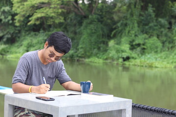 A handsome Asian man with black hair and glasses who dreams of becoming a book writer. Working off-site on holiday travel writing live with nature by the water with relaxation and peace of mind.