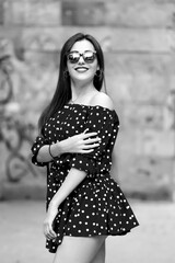 Portrait of a young beautiful fashionable elegant girl with long hair posing in the street. The model wears a stylish dress, sunglasses. Women's fashion concept