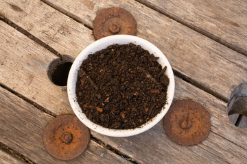 Gardening materials. Top closeup view of compost white bowl on the wooden table. Soil rich in minerals, and organic material.