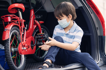 Fototapeta na wymiar A cute boy wearing face mask sitting in rear car with red bicyle preparing to ride at outdoor during pandemic of coronavirus covid 19.Social distance.