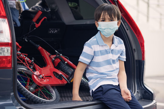 A cute boy wearing face mask sitting in rear car with red bicyle preparing to ride at outdoor during pandemic of coronavirus covid 19.Social distance.