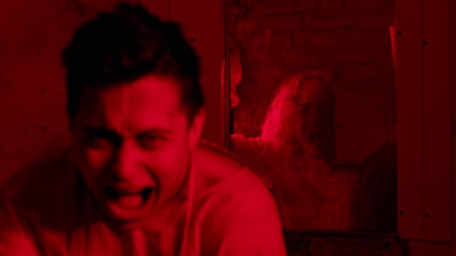 Crazy man sitting in the mental hospital in straitjacket and screaming with a scary girl on the background