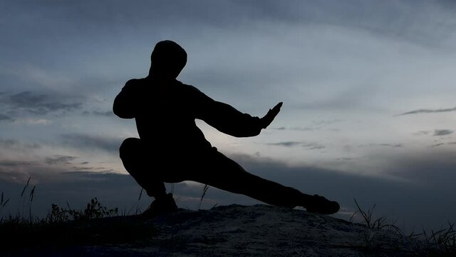 Silhouette of a man at sunset on the top of a mountain, a man practicing the art of Shaolin martial arts, a sports fighter training in nature. The young man is studying martial arts.