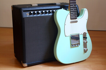 Turquoise electric guitar's bridge, pickup and strings leaning on amplifier