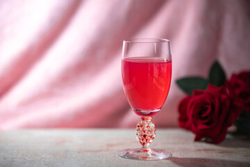 Pink collagen drink in a wine glass, placed on a wooden plank, a pink carpet background and a bouquet of roses.