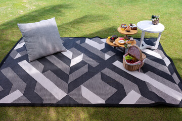 picnic set with small table with snacks and fruits basket on mat with pillow in garden on green...