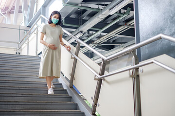 A Asian pregnant mother in a long dress was walking cautiously down the stairs.
