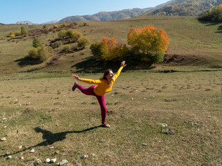 A woman in a good mood playfully makes a pose of a swallow in the mountains in autumn