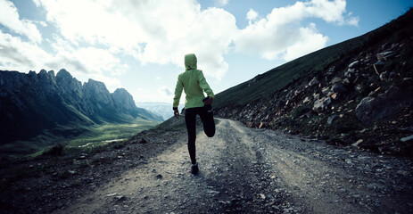 Woman ultramarathon runner stretching legs while running at mountain top
