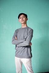 portrait of handsome asian man wearing gray t-shirt with cool pose. skinny man on green background. man folds hands on stomach with serious expression