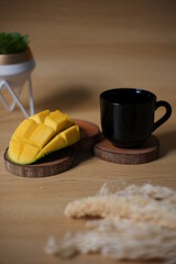 pieces of mango shaped like a blooming flower. fresh fruit and black cup on wooden background,