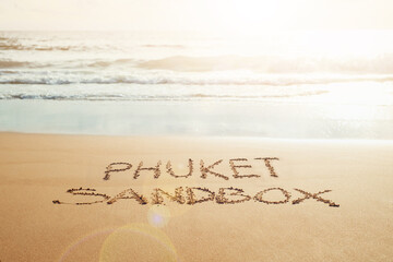 Phuket Sandbox text written in the sand on the beach in Phuket, Thailand with incoming wave