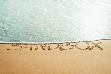Sandbox text written in the sand on the beach in Phuket, Thailand with incoming wave