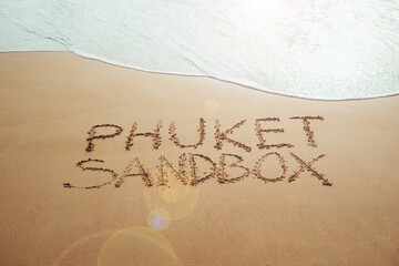Fototapeta premium Phuket Sandbox text written in the sand on the beach in Phuket, Thailand with incoming wave