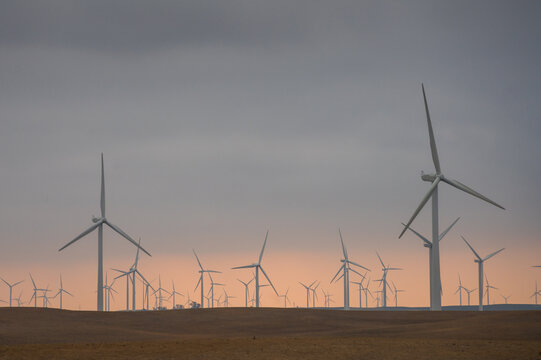 Dramatic image of a alternative power wind turbines on the fields of California valley with orange skies in the horizon.