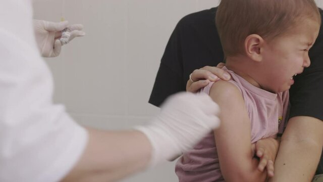 Doctor makes vaccination in the children's hands. Two years old kid crying while he is given an injection of a syringe in the shoulder close-up. 4k