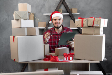 Happy Santa Claus working at the warehouse of goods in cardboard boxes for the holidays. Christmas gifts in Santa's workshop for the new year 2022. Delivers delivery.