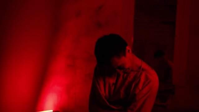 Mad man in straitjacket twitching and trying to get out of the clothes in the cell of mental hospital in red lighting