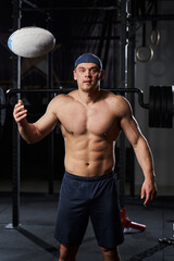 Fototapeta na wymiar Handsome muscled young man with a naked torso in the gym throws a ball for rugby