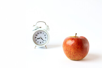 The concept of frequent fruit snacks during the working day. Red apple close-up on the clock background, light background, space for text