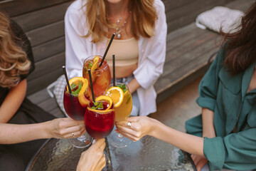Group of female friends cheers their drinks together, celebrating the first day of vacation.