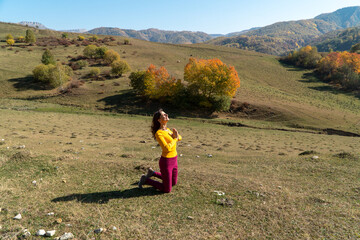 Fototapeta na wymiar Woman kneeling and looking at the sun with gratitude with namaste gesture, in autumn in the Caucasus mountains