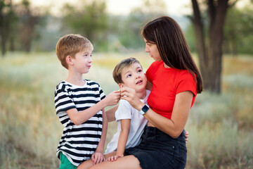 Candid authentic family portrait. Casual mom with two sons in confidential conversation In Rural Settings. Young woman with children on countryside background