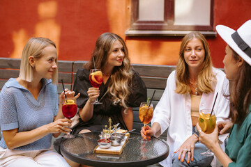 Happy diverse women clinking glasses of cocktails together in celebration while resting on terrace in summer.