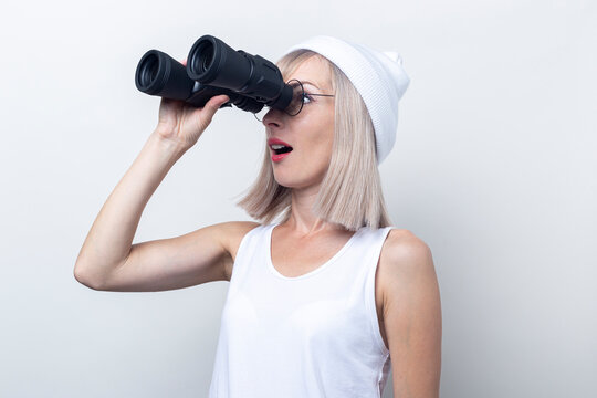 Surprised young woman looking through binoculars on a light background