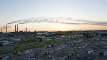 An epic sunset with a view of the smoke of the factory. There are garages and small houses. Near the beach of Lake Balkhash. There are many swifts and different birds flying. Ecology. Air pollution