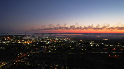 Fototapeta premium An epic sunset with a view of the smoking factory and the city. The embankment of Lake Balkhash. Low houses are standing and there are few trees. The pipes from the factory are smoking. Kazakhstan