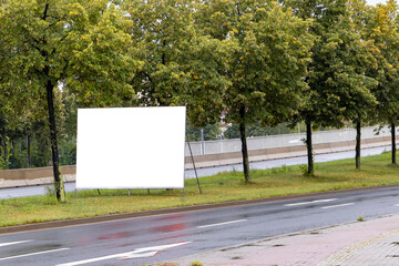A large billboard next to a road is available. Template for outdoor advertising. Empty billboard without people in the city. Space for an advertisement.
