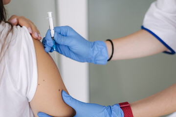 Close-up of female doctor in protective gloves holding syringe making covid 19 vaccination. Women getting injection in shoulder. Vaccine clinical trials concept, corona virus