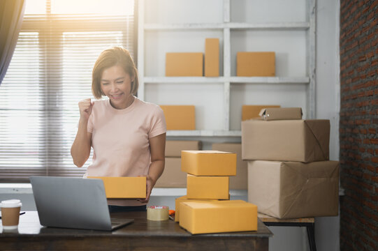 Happy young Asian woman entrepreneur, Smile for sales success after checking order from online shopping store in a smartphone at home office, Concept of merchant business online and eCommerce - Powered by Adobe