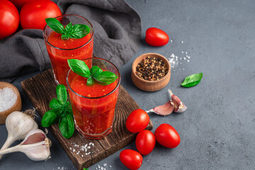 Two glasses of tomato juice, garlic, basil and spices on a gray-blue background. A healthy, organic drink.