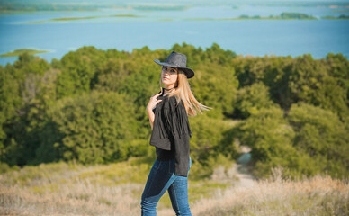 Girl in American country style black boho jacket with a fringe and cowboy hat at nature